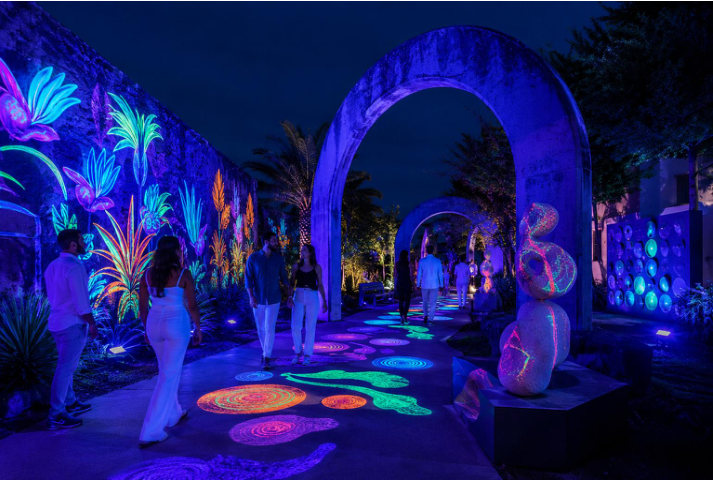 Night garden path under UV with fluorescent murals, stepping stones and an arch